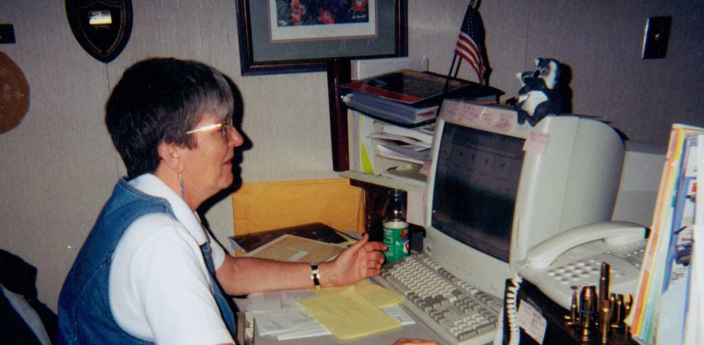 Brenda Potterfield looking at her computer, with many objects and documents on her desk.