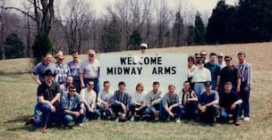 A group of people around a large white sign that reads Welcome Midway Arms.